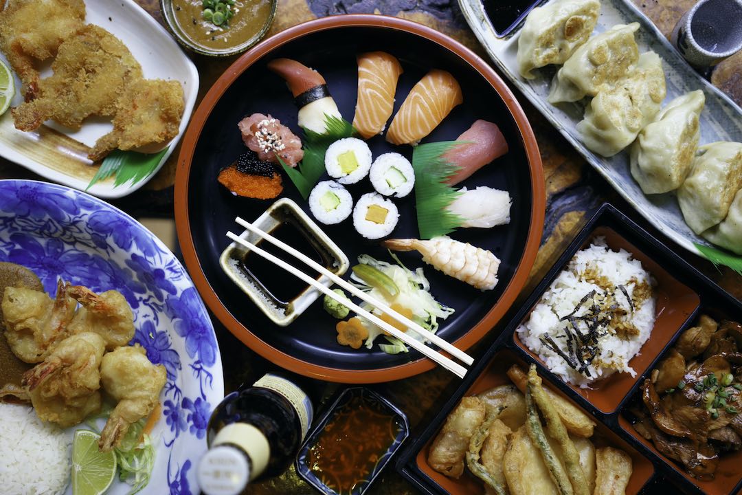 An overhead spread of sushi, tempura prawns, gyoza and bento boxes plated on dark wood at Little Tokyo Leeds
